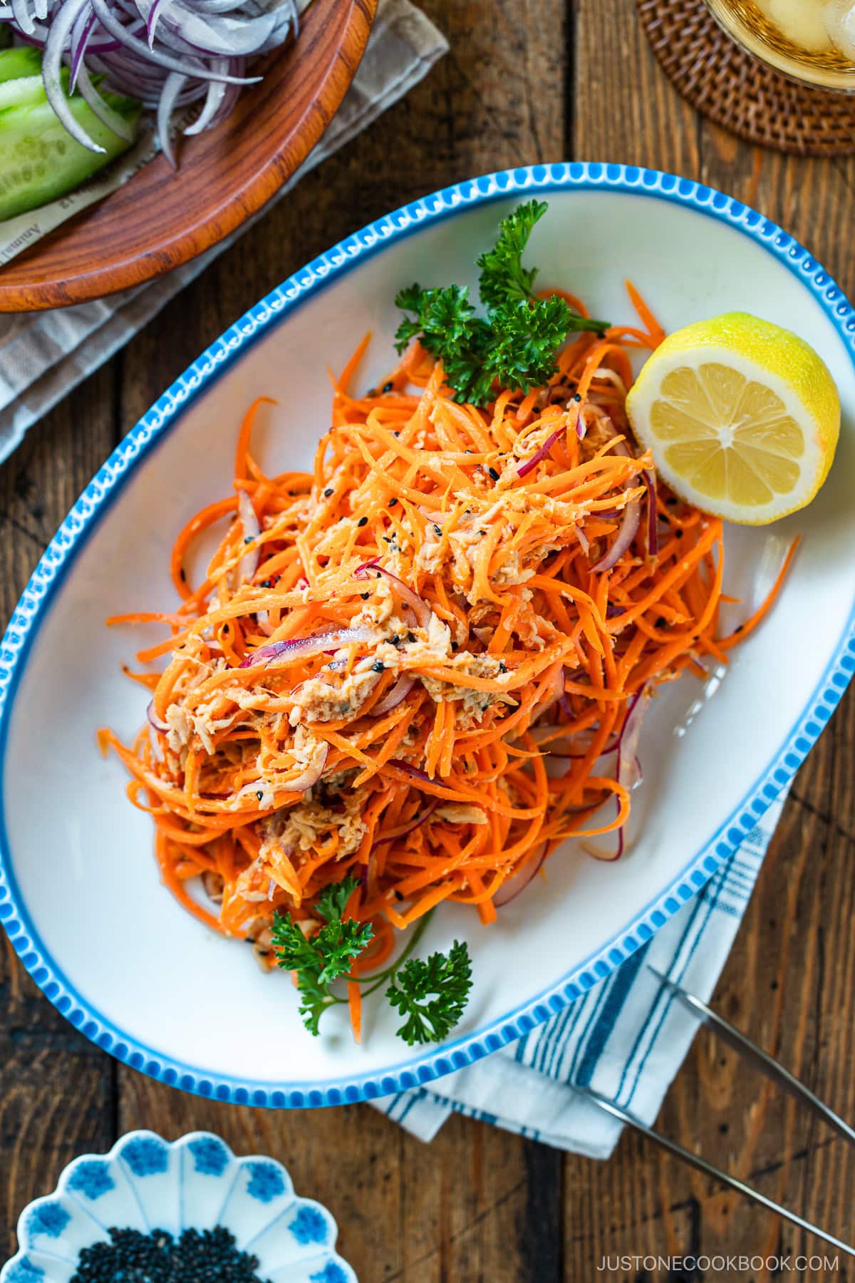 An oval scalloped plate containing shredded carrot and tuna salad garnished with parsley and lemon.