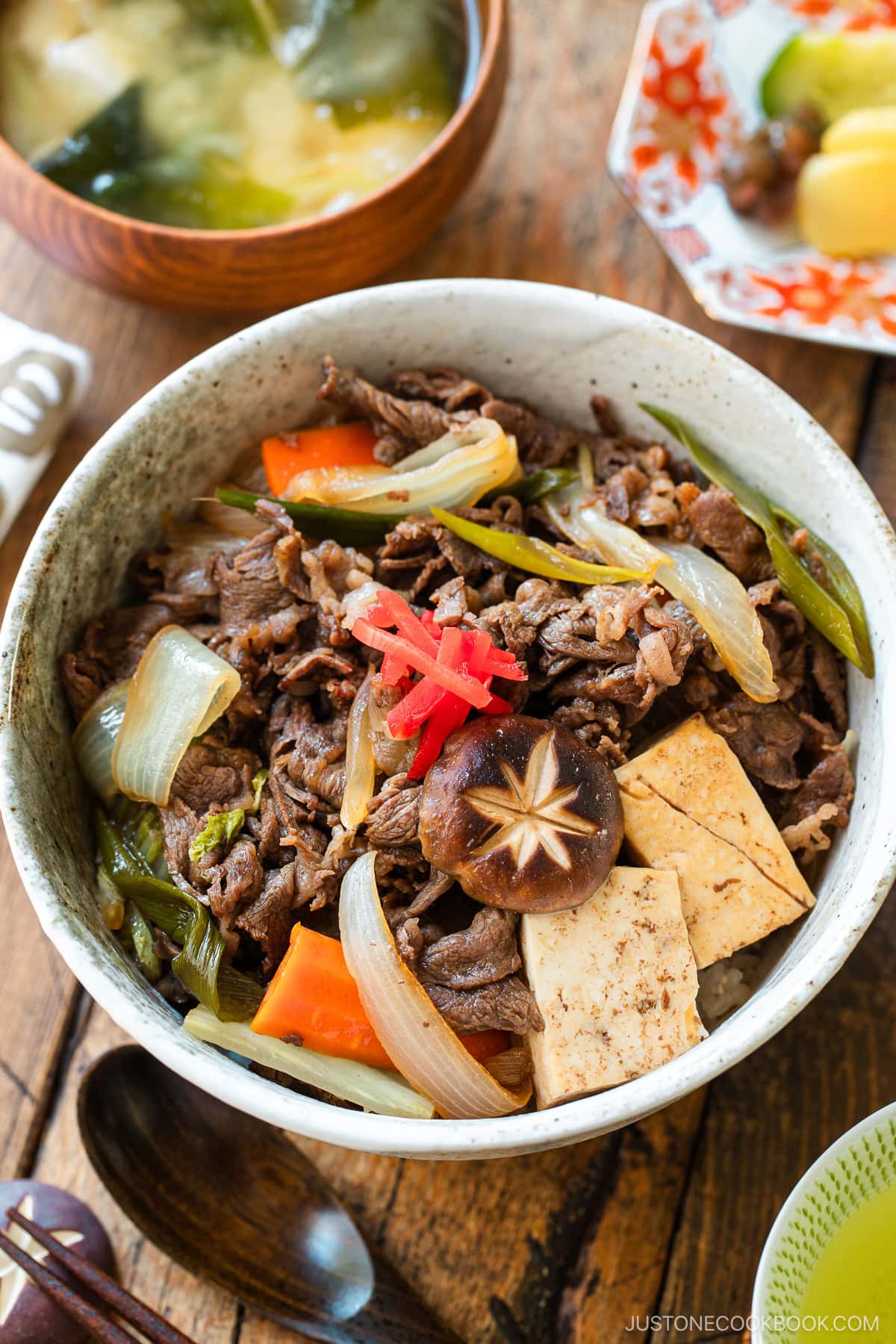 A large ceramic donburi rice bowl containing Sukiyaki Don, thinly sliced beef, tofu, and vegetables simmered in a savory dashi soy broth and served over steamed rice.